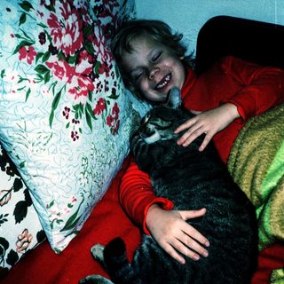 Child hugging a black cat on bed.