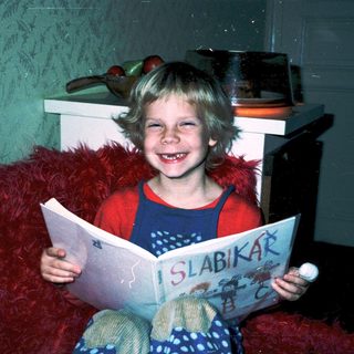 Child reading book titled "Slabikár" indoors.