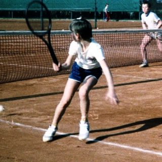 People playing tennis on outdoor clay court.