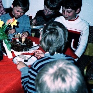 Children gathered around a table eating cake.