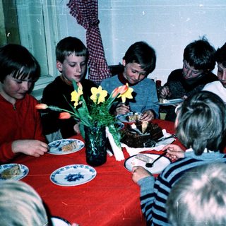 Children gathered around a table eating cake.