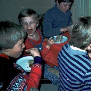Children gathered around a table eating cake.