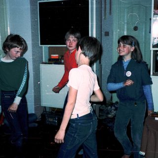 Four children playing indoors in a dimly lit room.