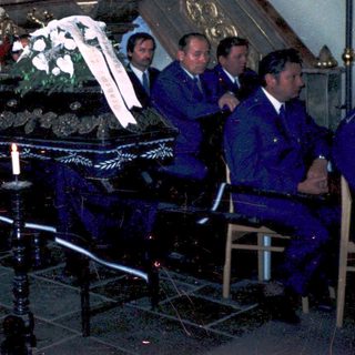 Funeral service with casket draped in flowers.