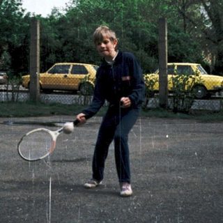 Person playing tennis in rain on outdoor court.