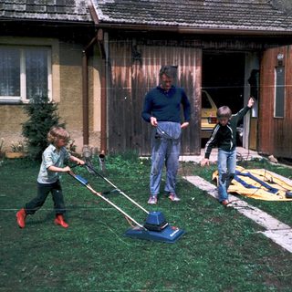 Family mowing lawn with children holding handles.