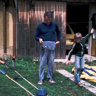 Family mowing lawn with children holding handles.