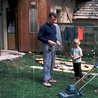 Family mowing lawn together outdoors in rain.