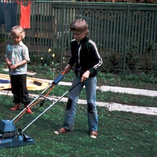 Family mowing lawn together outdoors in rain.