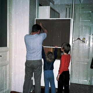Family installing large glass door panel together.