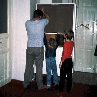 Family installing large glass door panel together.