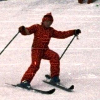 Skiers on groomed slope with onlookers.