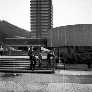 Modern building complex with rain-soaked plaza and people.