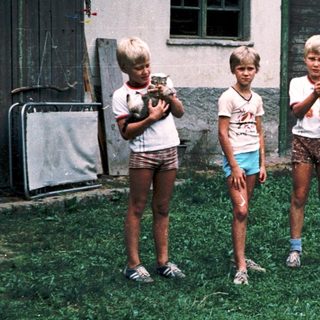Four children playing with toy guns outside old building.