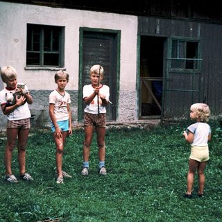 Four children playing with toy guns outside old building.