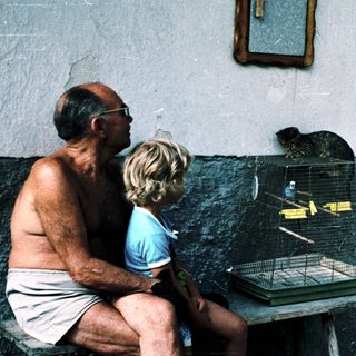 Two people observe a bird in a cage.