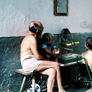 Three people playing table tennis outdoors near a building.