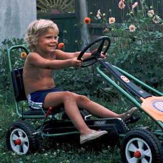 Young boy joyfully riding toy lawn mower.