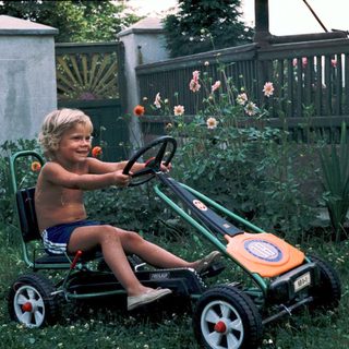 Young boy joyfully riding toy lawn mower.