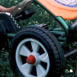 Young boy joyfully riding toy lawn mower.