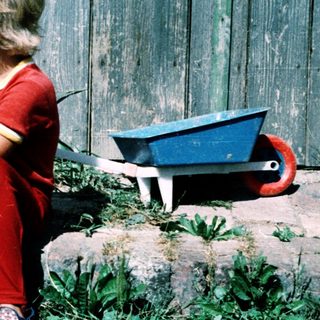 Young child sitting outdoors near toy wagon.