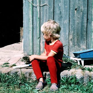 Young child sitting outdoors near toy wagon.