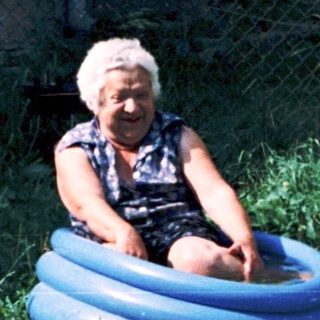 Old person sitting in inflatable pool outdoors.