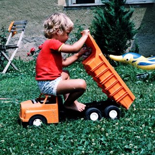 Child playing with toy dump truck outdoors.