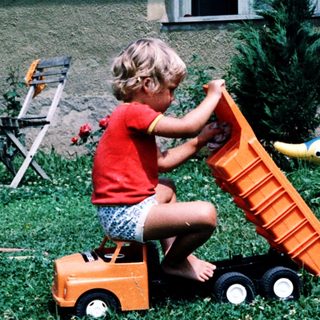 Child playing with toy dump truck outdoors.