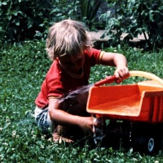 Child playing with toy tractor in grassy yard.