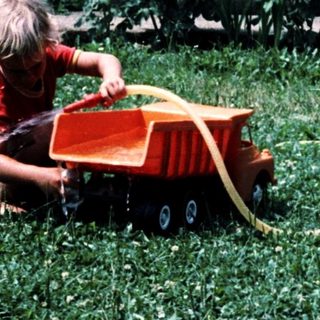 Child playing with toy tractor in grassy yard.
