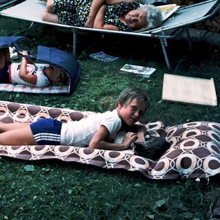 Children relaxing on camping mats outdoors.