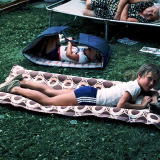 Children relaxing on camping mats outdoors.