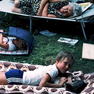 Children relaxing on camping mats outdoors.