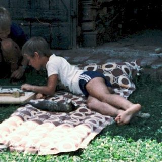 Children playing with a camera outdoors on blankets.