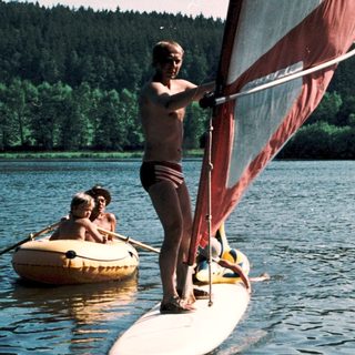 People windsurfing and paddleboarding on calm lake.