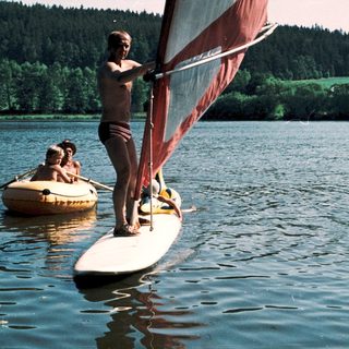 People windsurfing and paddleboarding on calm lake.