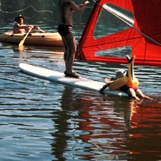 People windsurfing and paddleboarding on calm lake.