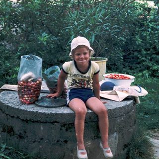 Child sitting on stone, holding cherry tomatoes.