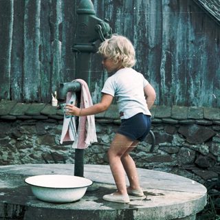Child pumping water from old outdoor hand pump.