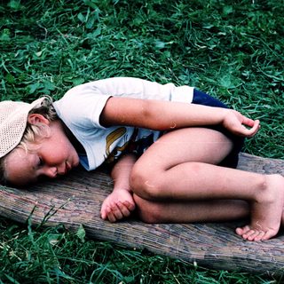 Child sleeping peacefully on wooden bench outdoors.