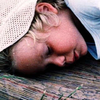 Child sleeping peacefully on wooden bench outdoors.
