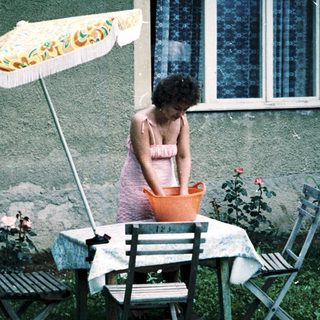 Woman sitting alone under umbrella at outdoor table.