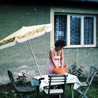 Woman sitting alone under umbrella at outdoor table.