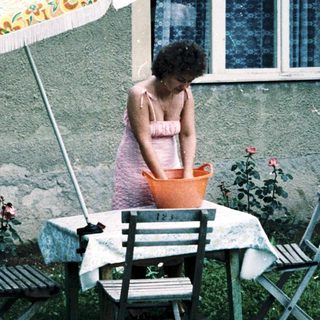 Woman sitting alone under umbrella at outdoor table.