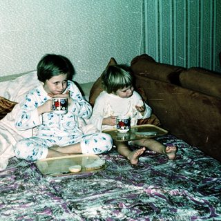 Two children in pajamas drinking hot chocolate on bed.