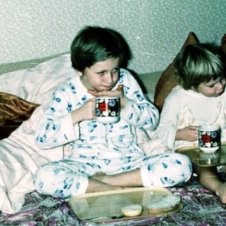 Two children in pajamas drinking hot chocolate on bed.