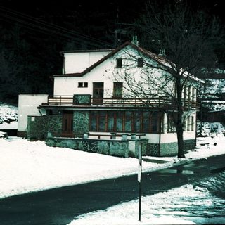 Snow-covered alpine house with parked vehicles.