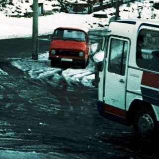 Snow-covered alpine house with parked vehicles.