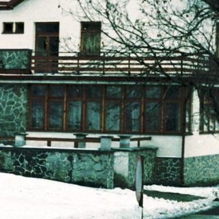Snow-covered alpine house with parked vehicles.